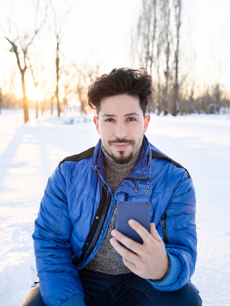 Uomo bello che guarda l'obbiettivo, utilizzando il telefono cellulare in una giornata di sole