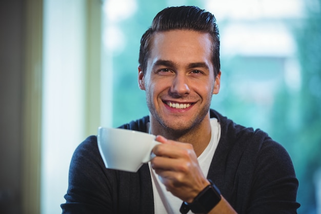 Uomo bello che ha una tazza di caffè in caffè