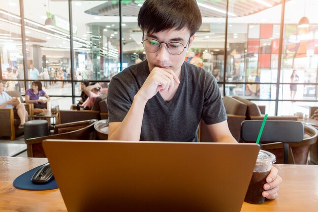 Uomo bello che lavora con il computer portatile del computer in caffetteria