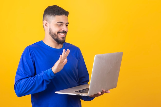 Uomo bello che lavora con il suo computer portatile su sfondo giallo