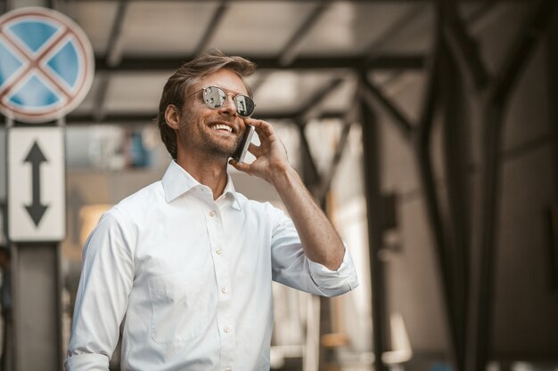 Uomo bello che parla sul telefono all'aperto con fondo urbano