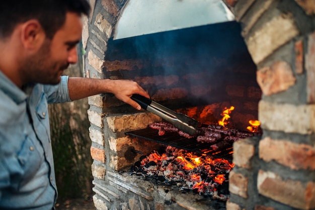 Uomo bello che prepara carne sul barbecue antiquato del mattone.