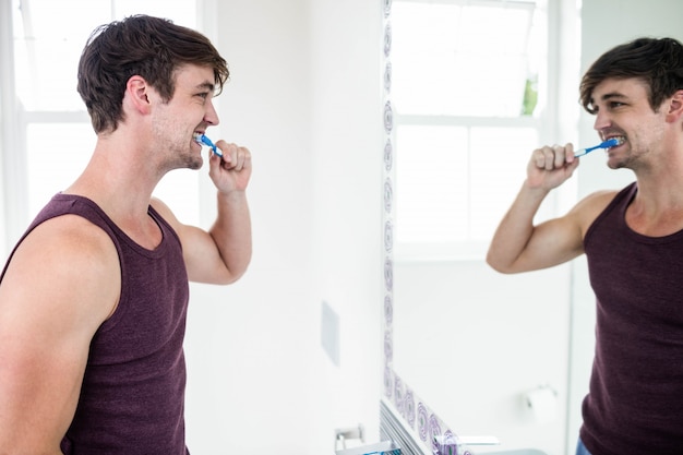 Uomo bello che pulisce i suoi denti in bagno