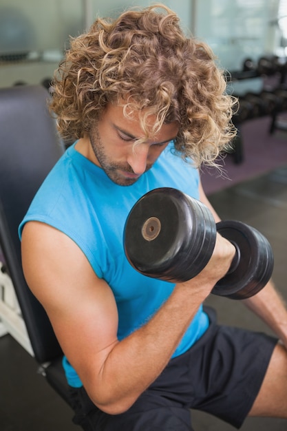 Uomo bello che si esercita con il dumbbell in ginnastica