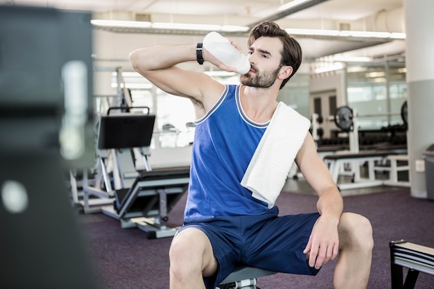 Uomo bello che si siede sulla trafilatrice che beve in palestra