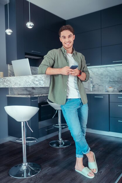 Uomo bello che sorride stando in piedi in cucina