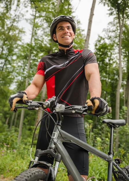 Uomo bello che sta con la bicicletta vicino alla foresta.