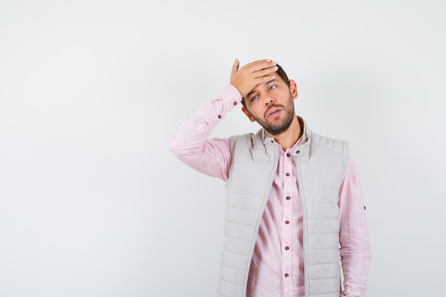 Uomo bello che tiene la mano sulla fronte in gilet, camicia e sembra pentito,