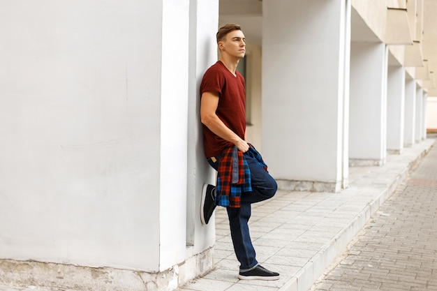 Uomo bello che tiene una camicia e posa vicino a un muro bianco