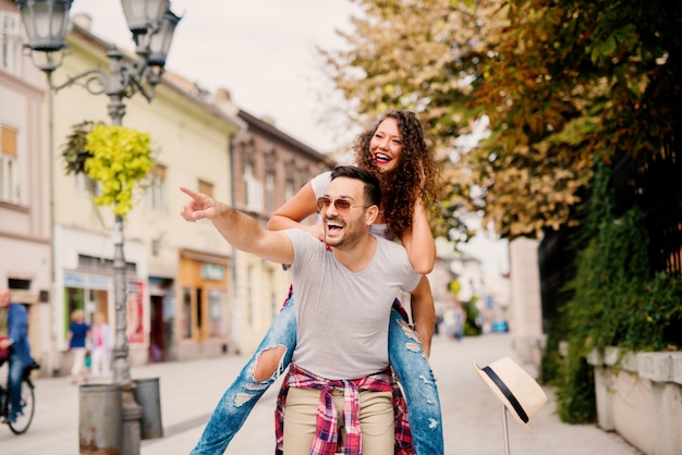 Uomo bello che trasporta bella ragazza con capelli ricci sulla schiena quando si cammina sulla strada.