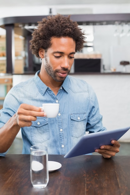 Uomo bello che utilizza compressa mentre mangiando caffè