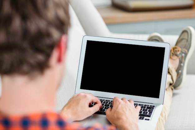 Uomo bello che utilizza computer portatile sullo strato a casa