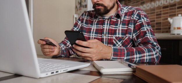 Uomo bello che utilizza la carta di credito per pagare online con lo smartphone