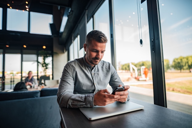 Uomo bello che utilizza smartphone nel caffè moderno.