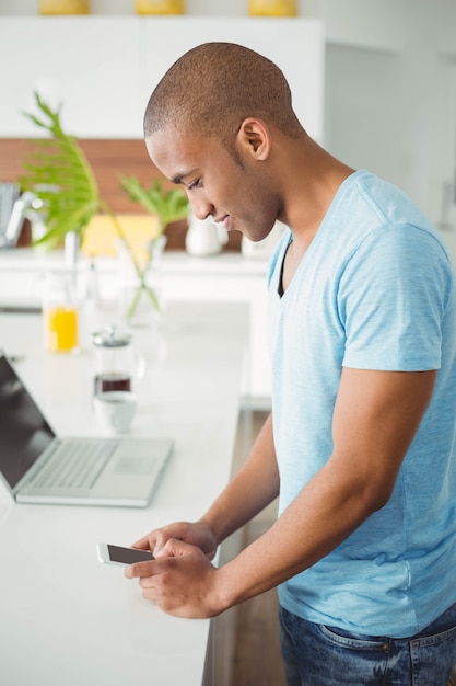 Uomo bello che utilizza smartphone nella cucina