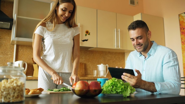 Uomo bello che utilizza tablet mentre la sua ragazza cucina