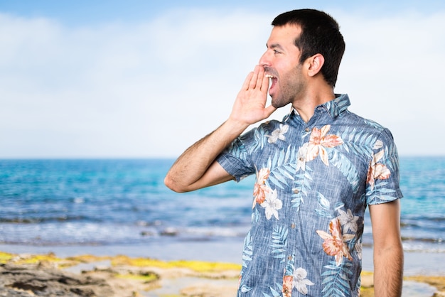 Uomo bello con camicia di fiori che grida sulla spiaggia