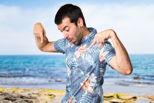 Uomo bello con camicia di fiori che punta verso la spiaggia