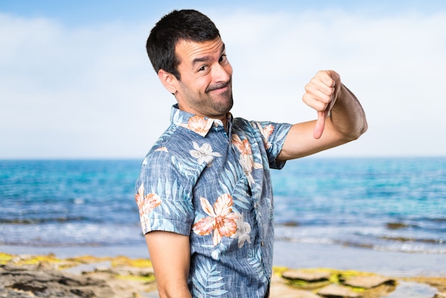 Uomo bello con camicia di fiori che rende cattivo segnale in spiaggia