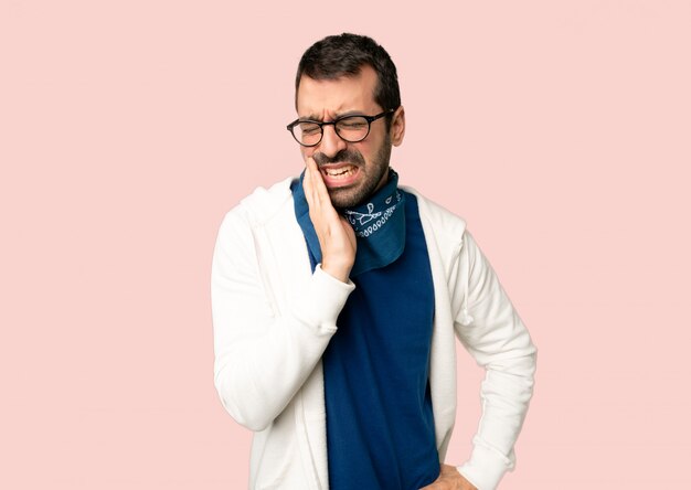 Uomo bello con gli occhiali con mal di denti su fondo rosa isolato