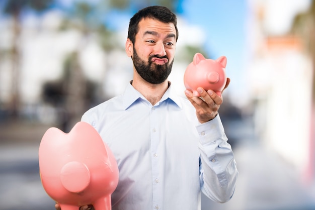 Uomo bello con la barba in possesso di un piggybank su sfondo unfocused