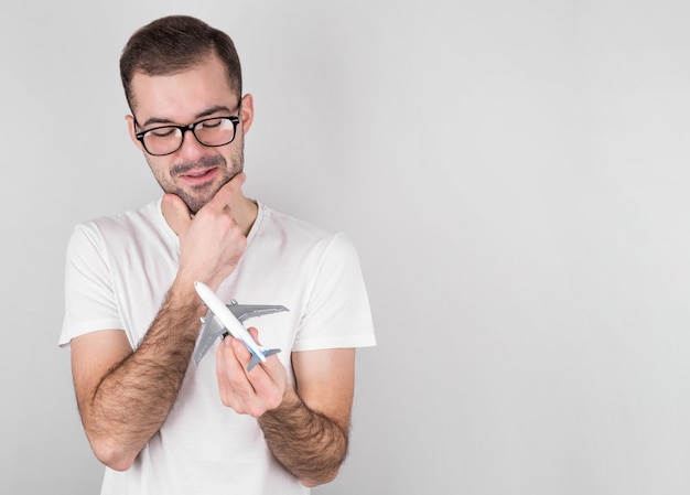 Uomo bello con la maglietta bianca che tiene aeroplano giocattolo sul muro grigio