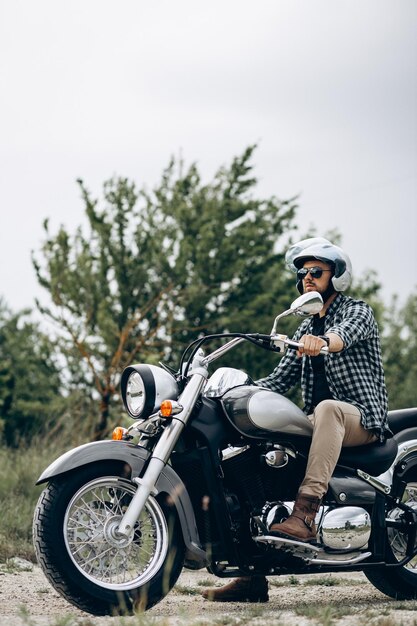 Uomo bello con la sua moto nella cava di sabbia