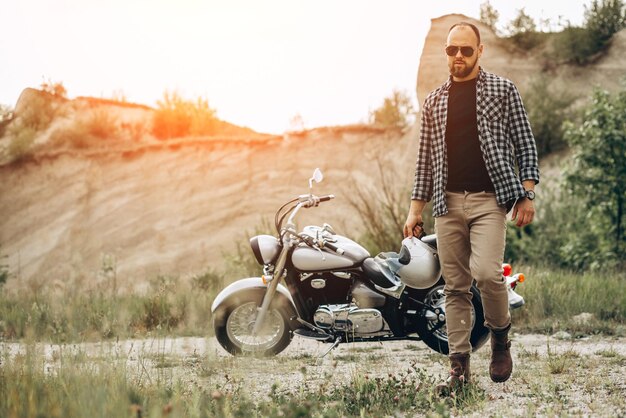 Uomo bello con la sua moto nella cava di sabbia