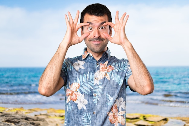 Uomo bello con una camicia da fiore che mostra qualcosa in spiaggia