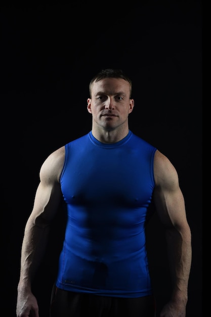 Uomo bello culturista o ragazzo muscoloso sexy in maglia blu con corpo atleta, torso e petto allenamento sport e posa in palestra su priorità bassa nera