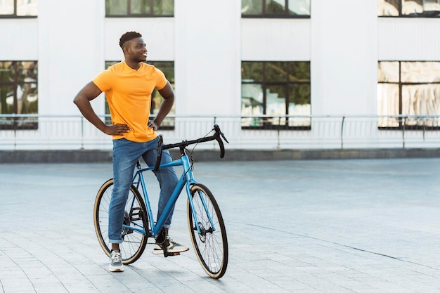 Uomo bello dalla pelle scura che cammina per strada vicino alla bicicletta mentre guarda via