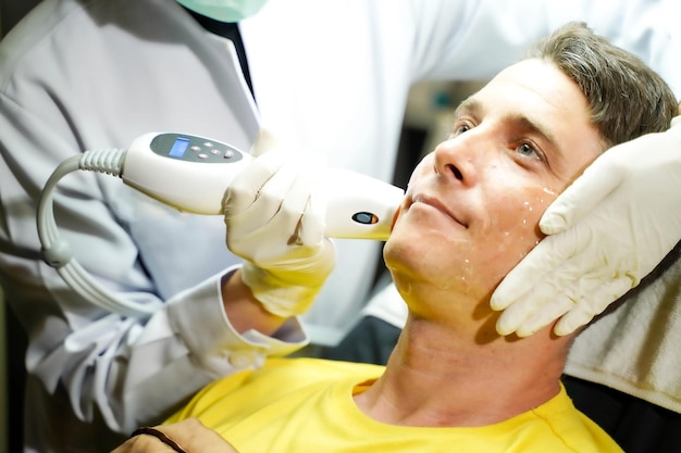 Uomo bello del primo piano che ha la terapia della luce del colore per stimolare il benessere della pelle del viso