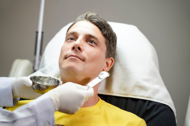 Uomo bello del primo piano che riceve il gel per la pelle per preparare la terapia della luce del colore per stimolare la salute del viso