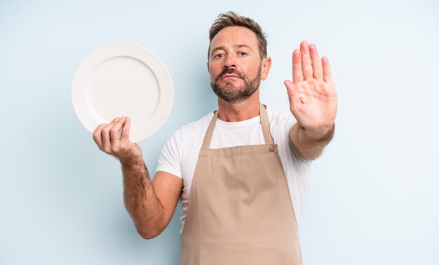 Uomo bello di mezza età che sembra serio mostrando palmo aperto che fa gesto di arresto. concetto di piatto vuoto