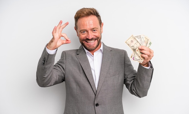Uomo bello di mezza età che si sente felice, mostrando approvazione con un gesto ok. concetto di banconote in dollari