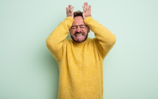 Uomo bello di mezza età che si sente stressato e ansioso, depresso e frustrato con un mal di testa che solleva entrambe le mani alla testa