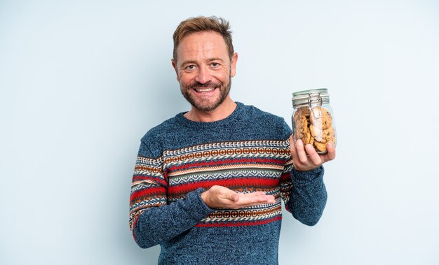 Uomo bello di mezza età che sorride allegramente, si sente felice e mostra un concetto. bottiglia di biscotti