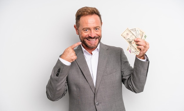 Uomo bello di mezza età che sorride con sicurezza indicando il proprio ampio sorriso. concetto di banconote in dollari