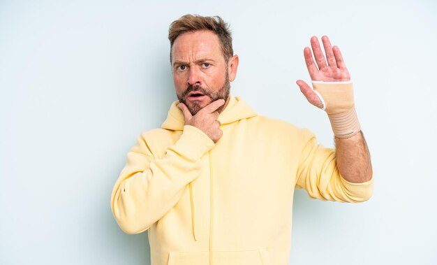 Uomo bello di mezza età con la bocca e gli occhi spalancati e la mano sul mento rotto il concetto di mano