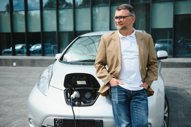 Uomo bello durante la ricarica dell'auto elettrica