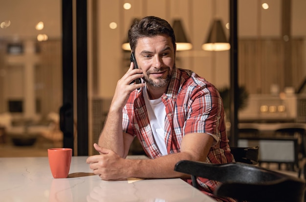 Uomo bello e allegro in casa sul divano che usa il cellulare Uomo attraente caucasico che si riposa sul divano nell'appartamento di notte che manda messaggi al telefono telefonico che naviga su Internet sullo smartphone