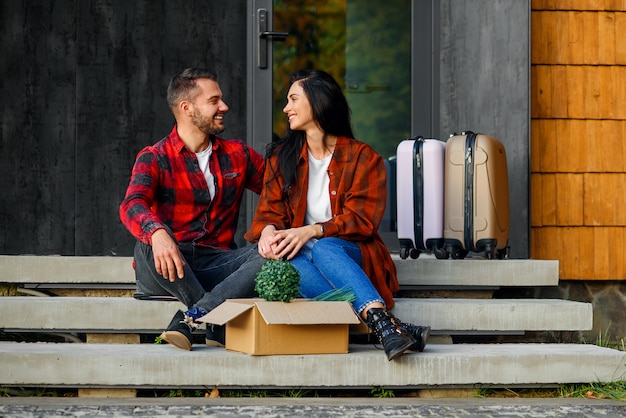 Uomo bello e bella giovane donna in vestiti alla moda che si siedono sui gradini della casa e che si guardano con amore durante il trasferimento nella nuova casa.