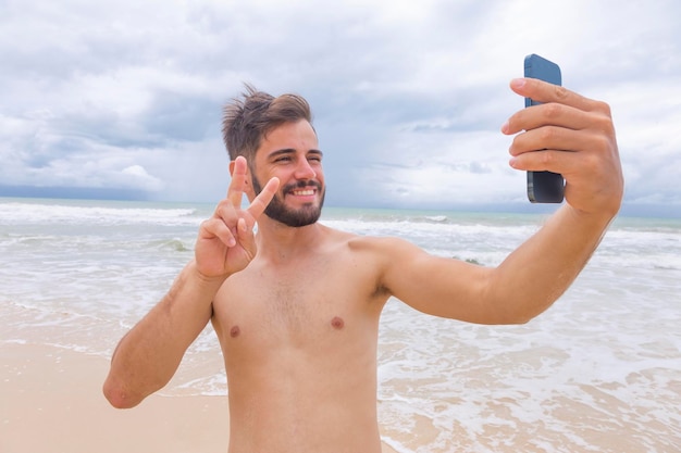 Uomo bello e felice che fa un selfie con lo smartphone in spiaggia Uomo in vacanza al mare che scatta foto con il cellulare