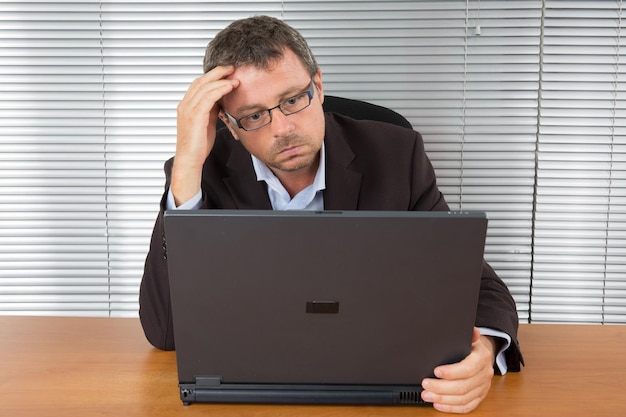 Uomo bello e serio con la barba lunga seduto a guardare direttamente il suo computer