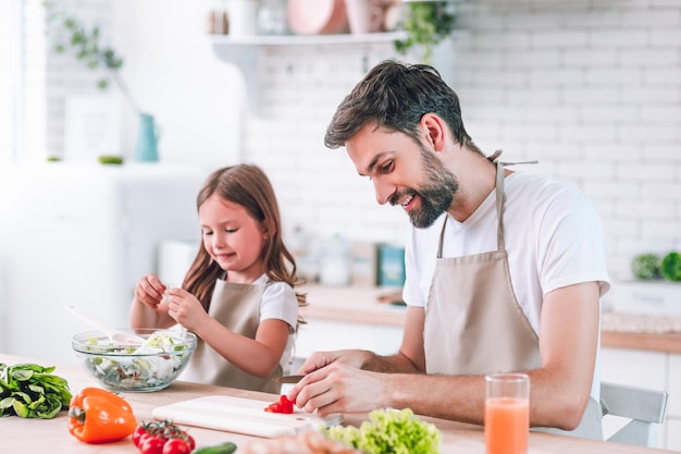 Uomo bello e sua figlia che preparano insieme l'insalata sulla cucina