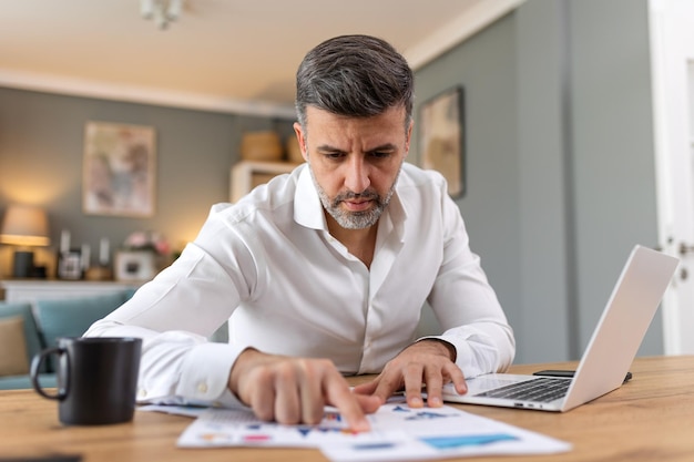 Uomo bello freelance che annota informazioni per la pianificazione di progetti che fa lavoro remoto tramite computer portatile Uomo che legge la posta elettronica su un moderno dispositivo portatile