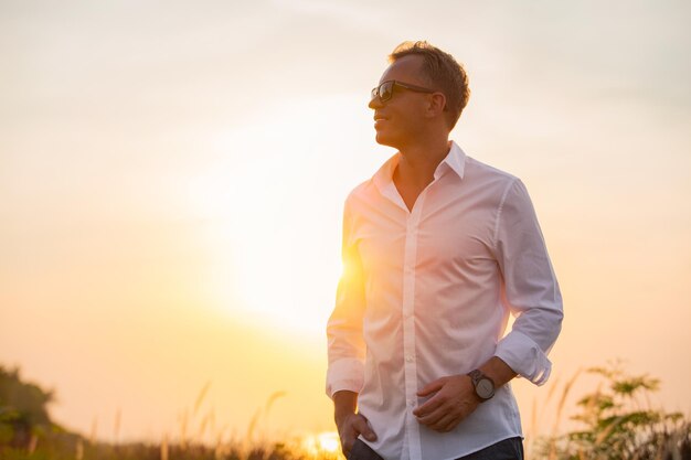 Uomo bello in camicia bianca in piedi al tramonto