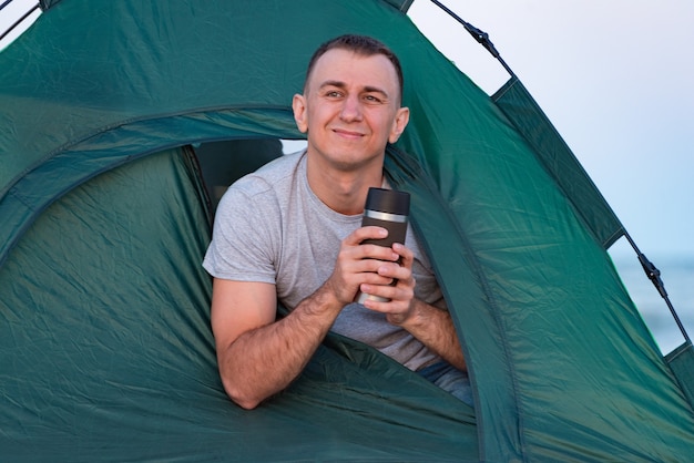 Uomo bello in una tenda turistica che tiene tazza termica