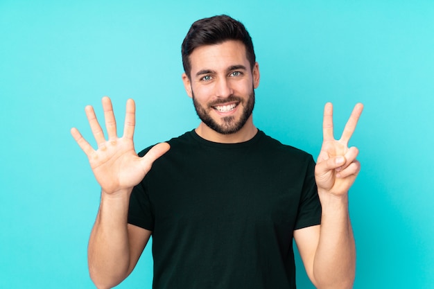 Uomo bello isolato sulla parete blu che conta sette con le dita