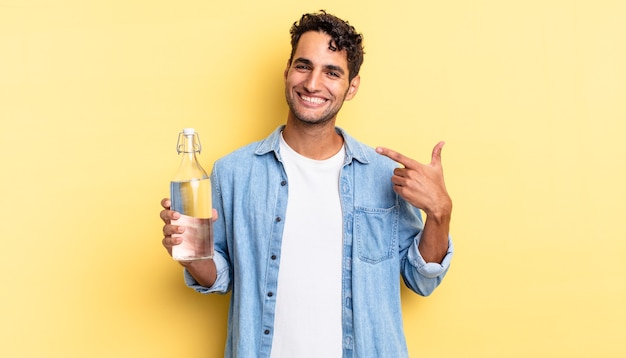 Uomo bello ispanico che sorride con sicurezza indicando il proprio ampio sorriso. concetto di bottiglia d'acqua